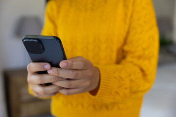 Midsection of biracial woman in yellow sweater using smartphone at home