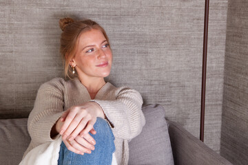 Chica rubia pelirroja sonriendo en la comodidad de su casa sentada en el sofá del salón con una...