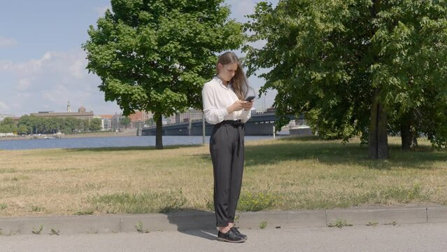 Business woman typing on smartphone in park on bright sunny day