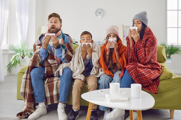 Achoo. Family of four have caught bad cold all together. Sick mom, dad and children in warm clothes and plaids sitting on couch in living room and sneezing in paper handkerchiefs. Winter, flu concept - obrazy, fototapety, plakaty