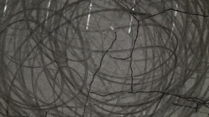 A top down shot over an empty parking lot. The camera tilted straight down, boom up and pan right showing tire marks from cars peeling out in circles. Taken on a sunny day.