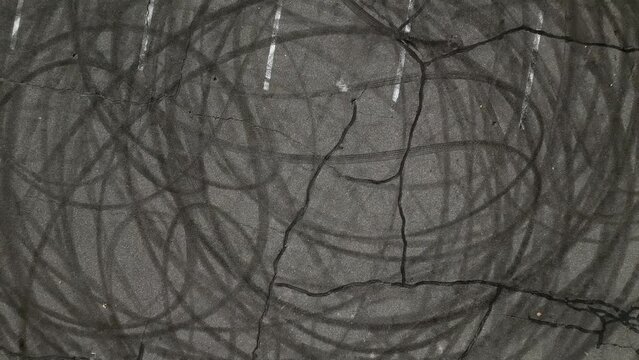 A top down shot over an empty parking lot. The camera tilted straight down, boom up and pan right showing tire marks from cars peeling out in circles. Taken on a sunny day.