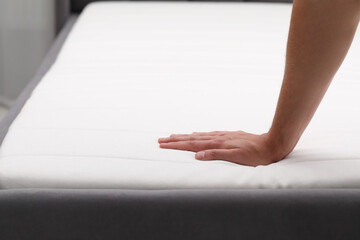 Man touching soft mattress with bed sheet, closeup