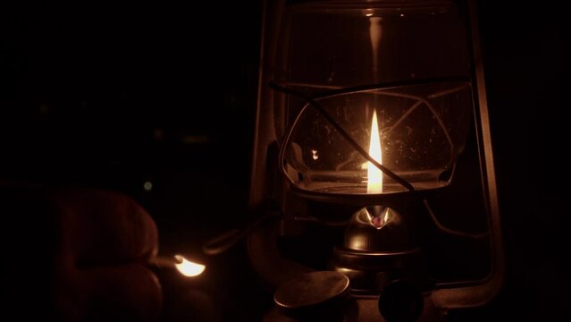 At dark night campsite, kerosene oil lamp is lit with burning match