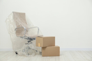 Modern office chair covered with plastic film and boxes near white wall indoors. Space for text