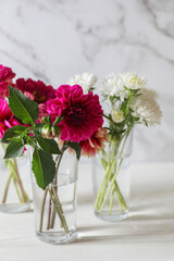 Bouquet of beautiful wild flowers and leaves in vases on white wooden table against marble background