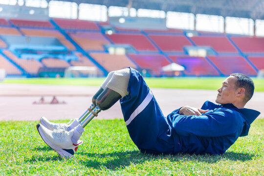 Asian para-athlete with prosthetic blades leg in stadium practicing workout for Paralympic running competition. Amputee sportsman runner practicing running workout. Disabled athlete man sport concept.