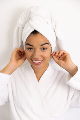 Portrait of happy biracial woman in bathrobe and with towel against white wall