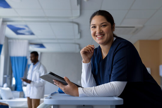 Portrait of happy biracial female doctor holding tablet in sunny hospital room