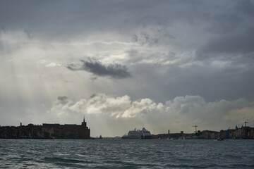 Obraz premium Sun rays and dramatic clouds at the entrance to Venetian lagoon on Guidecca canal. Venice - 4 May, 2019