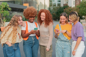 Group of happy female friends looking at their mobile phones showing the last funny and...