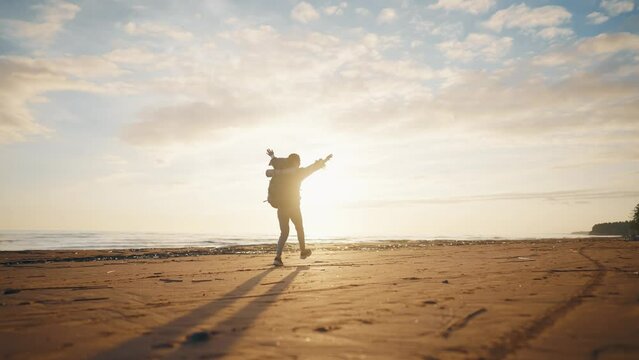 Happy woman skipping on sand sea beach. Female tourist rejoicing vacations walking along ocean jumping turning feeling freedom. Hiker carrying touristic backpack. Tourism travel wanderlust concept.