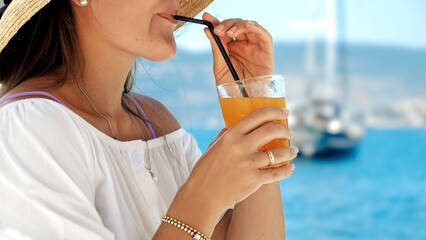 In a beach cafe gazebo on the pier, brunette woman enjoys her orange juice. Essence of summertime,...