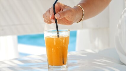 At a beach cafe, a woman stirs her orange juice with a straw, capturing the essence of summertime,...