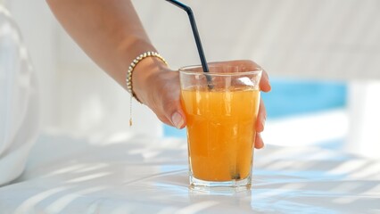 Delighted brunette woman enjoys her orange juice at sea beach cafe. Essence of summertime, holiday escape, relaxation, and wanderlust