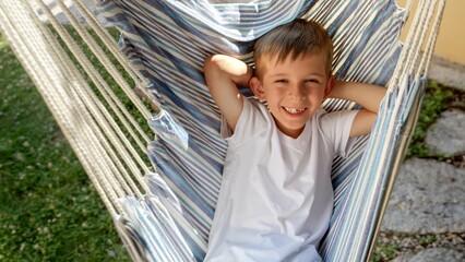 Happy smiling boy swinging and lying in hammock at garden. Summertime, happy childhood, vacation