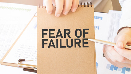 Text FEAR OF FAILURE on brown paper notepad in businessman hands on the table with diagram....