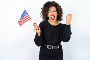 Young beautiful woman with curly hair wearing black dress and holding and American USA flag and...