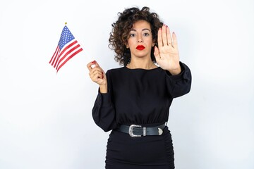 Young beautiful woman with curly hair wearing black dress and holding and American USA flag and...