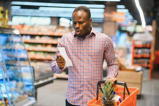 Surprised African-American man looks at receipt total in sales check holding paper bag