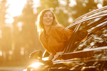 A young woman enjoys the sunny weather from the car window. Happy tourist travels by car. Adventure...