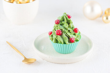 Vegan cupcake in the form of a Christmas tree with coconut cream, spirulina, cranberries and Christmas toys. Gluten, lactose, sugar free.