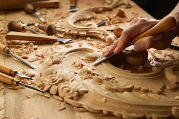 Hands of craftsman carve with a gouge in the hands on the workbench in carpentry. Wood carving tools close-up - obrazy, fototapety, plakaty