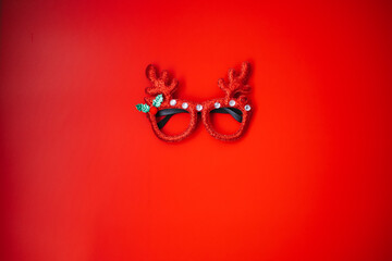 Christmas masquerade glasses with deer antlers on a red background. The concept of a Christmas party. A fun holiday. Decoration for children and adults. - obrazy, fototapety, plakaty