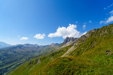 Fototapeta premium Eine weite Berglandschaft mit saftig grünen Hängen erstreckt sich unter einem strahlend blauen Himmel mit vereinzelten weißen Wolken.