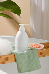 Pump bottle in white color decorated with a bath sponge and a small dish of pink himalayan salt. White cosmetic bottle for face cream, cleanser, body lotion or shampoo
