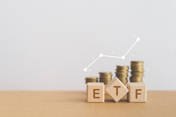ETF abbreviation for Exchange Traded Fund written on wooden cube blocks with blurred stack of coins...