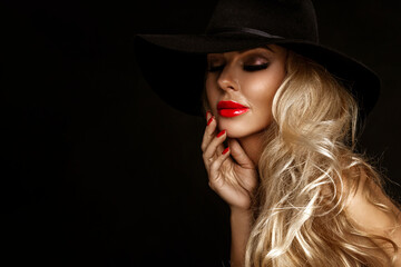 Beautiful woman in elegant makeup with red lips and nails posing sensually on a black background.