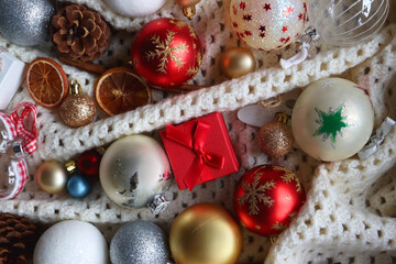 Various colorful Christmas ornaments, small presents and seasonal spices on white knitted blanket. Top view.