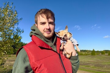 Portrait of happy young man with his Chihuahua dog, hold on hands little puppy on natural...