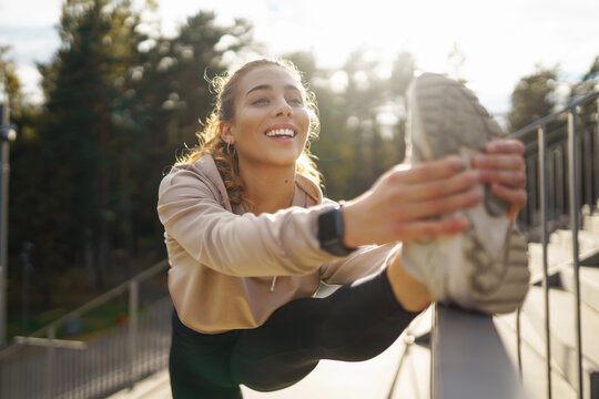 Young woman in sportswear is training outdoors. Fitness woman with smart watch goes in for sports, performs stretching exercises. Sports concept, healthy body.