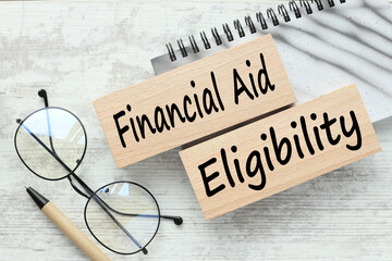 Financial Aid Eligibility. gray notepad with text on wooden blocks