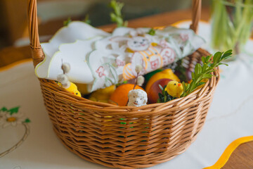 Traditional Easter basket on family table in Poland. Easter modern eggs, easter bread, ham, beets, butter, in wicker basket decorated with green boxwood branches and flowers on rustic wooden table