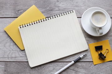 Blank notepad on yellow notepad and cup of coffee on wooden table in office - Powered by Adobe