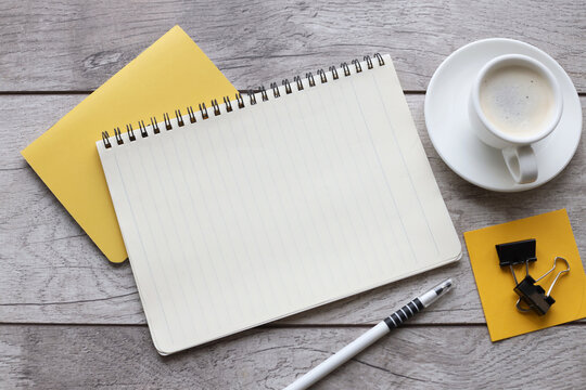 Blank notepad on yellow notepad and cup of coffee on wooden table in office