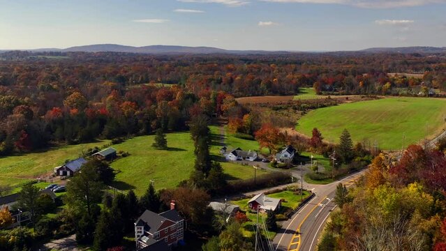 A high angle aerial view over the quiet countryside of New Jersey with colorful trees and large green fields all around on a sunny day in autumn. The camera dolly in and pan right over the scenery.