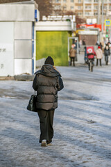 A woman with a bag walks along the sidewalk on an autumn day