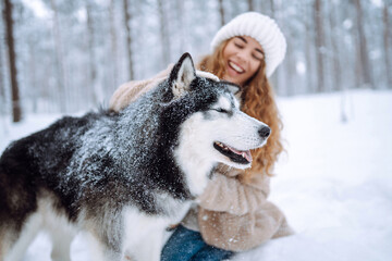 Beautiful young woman walks through the winter forest with her dog. A young woman with her pet on an adventure. Friendship concept, pets. Friendship between a woman and a dog. 