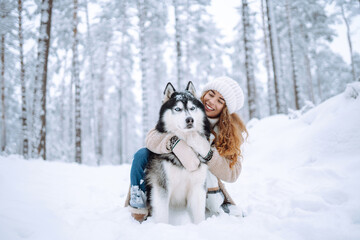 Beautiful young woman walks through the winter forest with her dog. A young woman with her pet on an adventure. Friendship concept, pets. Friendship between a woman and a dog. 