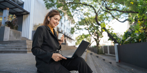Smiling young Asian business woman using laptop sitting outdoor. hybrid working, searching job online thinking of digital solution