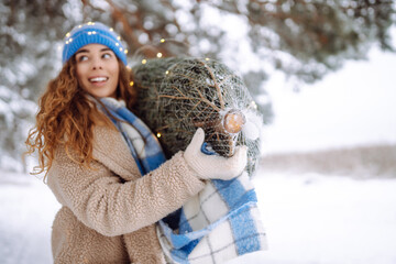 Happy woman carries a Christmas tree through a snowy forest. A young woman enjoys the preceding...