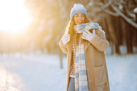 Laughing beautiful woman in the winter forest enjoying an amazing sunset. Great mood on the first snow. The girl is dressed in a fur coat, hat, and scarf. Walking concept.