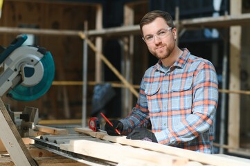 Skilled cabinet maker cutting wood board with electric circular saw at woodworking sawmill....