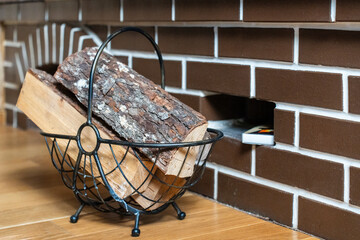 Black metal log holder filled with several pieces of firewood. It's situated on a wooden floor, in...