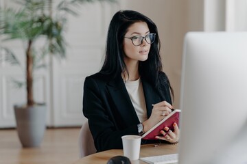 Concentrated journalist jotting down notes in a paper notepad, with computer and coffee in office