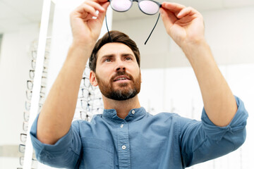Stylish man with beard choosing glasses in the optics
